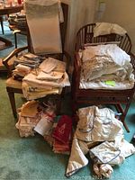 Photo showing multiple stacks of assorted tablecloths, napkins, and cloth items piled on and beside chairs.