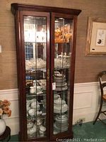 Front view of wooden curio cabinet showing glass shelves with various glassware inside.