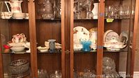 View of cabinet middle shelf with various glass and porcelain dishes, bowls, and vases.
