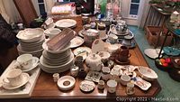 Wide view of assorted porcelain and china dishes, bowls, cups, and decorative items arranged on a wooden table.
