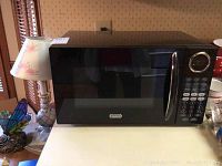 Front view of black Sunbeam microwave placed on countertop next to lamp and other kitchen items.