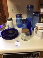 Wide view of all items including deep blue plates, blue canisters, white ceramic canisters, vase, and clear glasses in American Brilliant design by Libby.