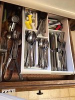 Drawer with sorted flatware including spoons, forks, knives, and kitchen tools such as plastic lemon squeezers and cheese knife.