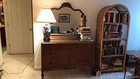 Full view of antique wooden dresser with a lamp on top and large attached mirror reflecting part of the room.
