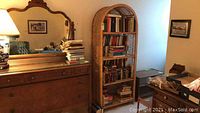 Full view of wicker rattan bookcase next to dresser and mirror with books on shelves.
