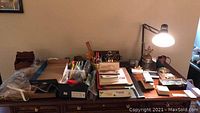 Wide shot of office supplies including desk lamp, barometer, pen sets, and boxes of miscellaneous supplies on table.