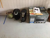 All items shown side by side on floor, including Rival crock pot, Keurig coffee maker, Mr. Coffee coffee maker, and boxed Panasonic microwave.