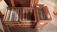 Wooden rack and cardboard box filled with numerous vinyl records from various artists.