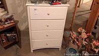 Front view of white chest of drawers with four drawers and round knobs, showing overall condition and size.