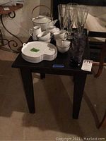 Black small table with clean lines and square legs. Items on top are various dishes and glassware, not included.