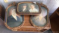 Three convex glass framed vintage portrait prints, two wood framed with floral carvings, one composite frame showing mature couple.