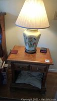 Night stand with drawer topped with glass floral lamp and lampshade, shown lit.