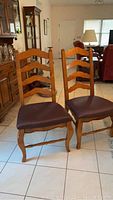 Two wooden dining chairs with ladder backs and brown cushions in a room with other furniture.
