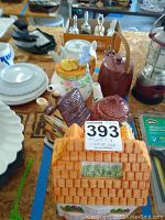 Wide shot of multiple ceramic teapots and cookie jar arranged on table, showing teapots of different colors and styles and the house-shaped cookie jar