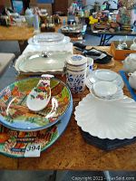 Full view showing several platters and dishes including colorful ceramic plates, glass casserole, blue and white cannister and white shell dishes.