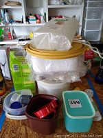 Stacked plastic food containers, a cracker keeper, a pack of foam plates on top, and a brown and red plastic bucket container.