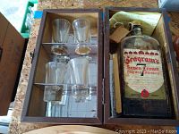 Wooden case with four clear glass whiskey glasses and vintage Seagram's Seven Crown whiskey bottle with label.