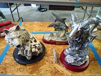 Three animal figurines: silver ram by Herco, dolphin figurine, and wolf head bust on round base.