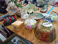 Wide view of various Asian decorative bowls, jars, fan and other items on a table.