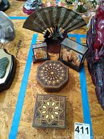 Wide shot showing all items including two mother of pearl inlaid wooden boxes, two cork display cases, and brass fan on stand, with surrounding objects visible.