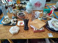 Wide shot of assorted decor items on wooden table showing plates, figurines, glassware, vases, covered dish, and various collectibles.