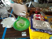Wide view of table showing Fenton ruffled basket, green glass bowl, hand painted teapot, and assorted other items including rain gear.