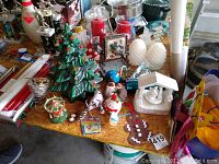 Overview of assorted Christmas decorations including ceramic tree, music box, LED pine cones, candles, snow globe, and wrapping paper