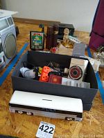 Full view of lot items including a black box with assorted tools and electronics, cassette player, and cologne bottles placed on the floor.