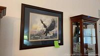 Framed picture of a flying bald eagle over a landscape, black and gold frame, hanging on a wall.