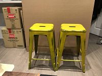 Two yellow metal counter height stools side by side showing wear marks as part of industrial style.