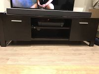 Front view of modern media console TV stand showing two closed side cabinets with metal handles, open shelf in center, and flat top surface with soundbar on top.