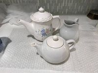 Photo showing two ceramic teapots and one creamer on a bubble wrap surface with a tiled backsplash.