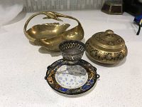 Brass swan candy dish, brass round lidded dish, and a small brass item on white counter