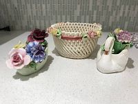 Three bone china items including a swan figurine, a woven ceramic basket with floral accents, and a green flower pot milker with flowers.