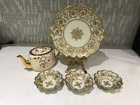 Full view of the antique NIPPON porcelain set including teapot, large plate on stand, and three small dishes with gold hand-painted floral designs.