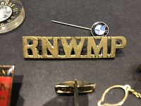 Close-up photo of Royal North West Mounted Police pin and BMW round logo pin on black background.