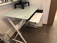 Side angle of work desk showing frosted glass top and keyboard tray underneath with X-brace white steel frame.
