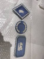 Top view of three Wedgwood blue jasperware pieces (one square tray, one round ashtray, one rectangular tray) on bubble wrap.