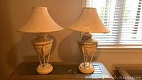 Pair of two textured pottery finish lamps with beige fabric lampshades on a wooden surface