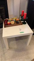 White melamine Parson's table holding wooden tray with 9 novelty candles and 3 green glass candle holders with red candles.