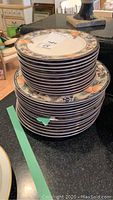 Stack of Mikasa Intaglio china plates showing floral and fruit pattern with chip on one plate badge with green tape for identification