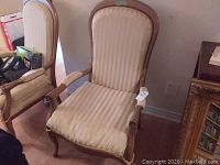 Front view of beige fabric occasional chair with vertical stripes upholstery and composite wood frame with carvings.