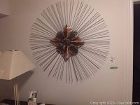 Wide view of the metal wall art mounted on a white wall next to a lamp and some boxes, showing full size and placement.