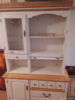 Front view of two-piece hutch cabinet showing glass door on the upper hutch, drawer below, open shelving compartments, three drawers, large drawer, and cupboard in lower cabinet with natural wood top.