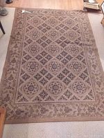 Full view of the rectangular area rug showing the beige and light brown tones with floral and geometric patterns inside the border