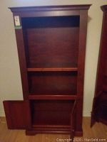 Front view of the solid cherry wood bookcase showing open shelves and lower cupboard with door open.