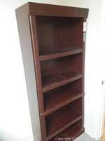Front view of the tall dark brown laminate bookcase with three shelves and visible wear marks on shelves.