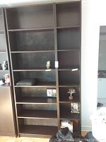 Front view of two tall dark brown laminate bookcases with several adjustable shelves, some shelves holding small decorative items.