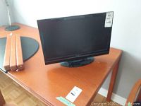 Black Insignia LCD monitor on wooden desk along with a metal adjustable desk lamp.