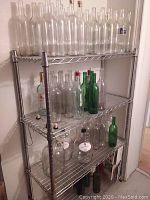 Photo of assorted empty glass bottles and jugs on a metal shelving rack, showing various sizes and colors including clear and green glass bottles.
